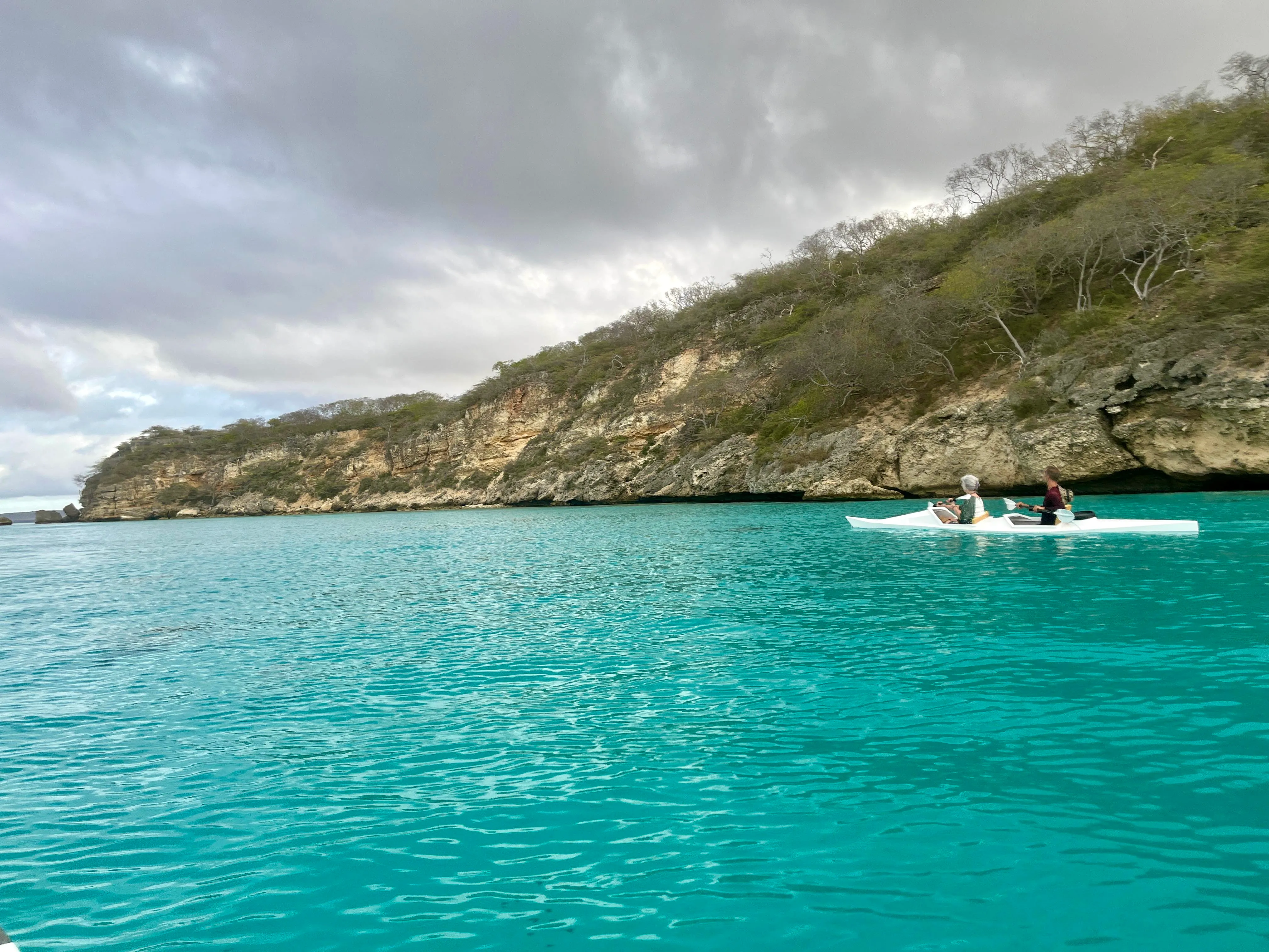 Two paddlers in a kayak on the turquoise water below Curaçao's limestone cliffs